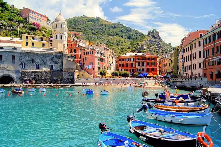 Vernazza harbor in Cinque Terre with colorful boats and historic architecture against a scenic hillside backdrop.