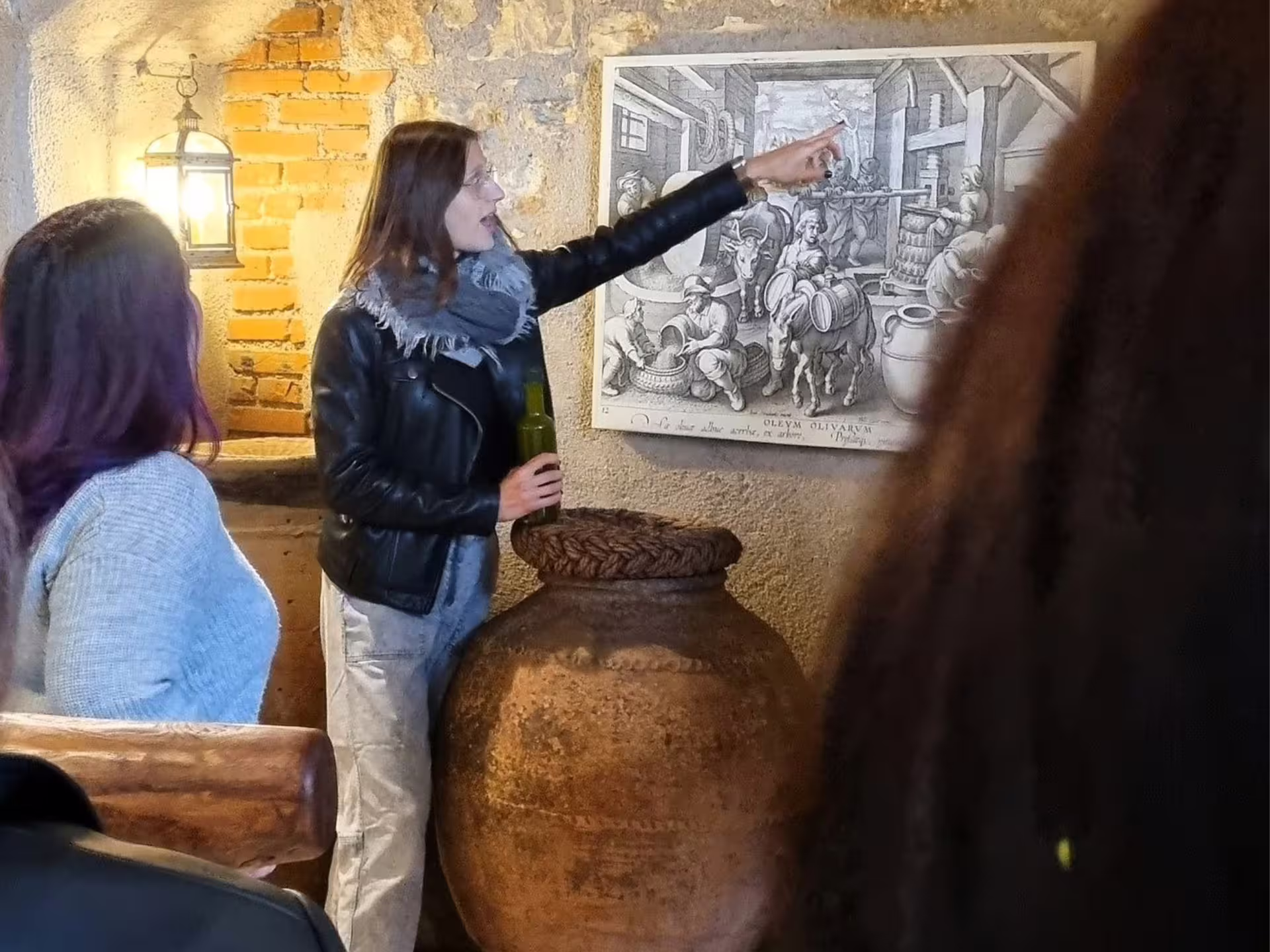 Guide explains olive oil heritage beside antique jar during Verona countryside olive mill tour and tasting