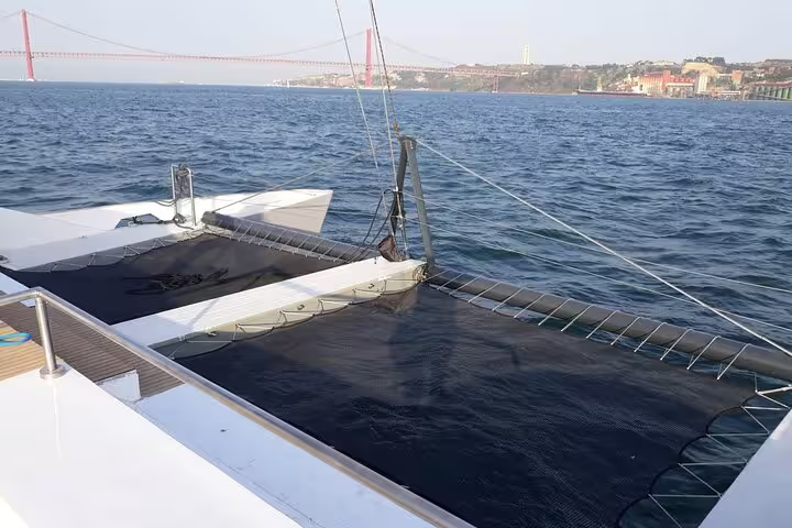 View from the Vertigo catamaran showcasing Lisbon's iconic red bridge under clear skies, perfect for a sailing adventure.