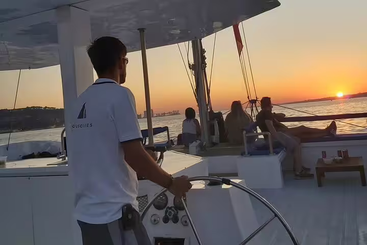 Captain steering the Vertigo catamaran at sunset, with passengers enjoying a scenic 2-hour private tour in Lisbon.