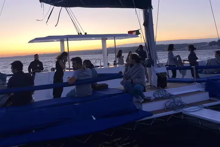 Guests enjoy a sunset view on the spacious deck of the Vertigo catamaran during a private sailing tour in Lisbon.