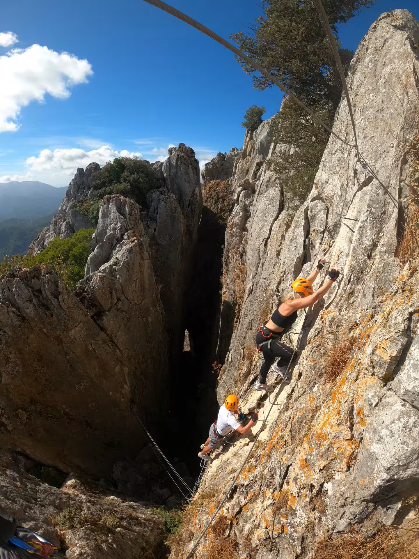 Two climbers on rugged rock face enjoying panoramic views during Via Ferrata adventure in Benalauría.