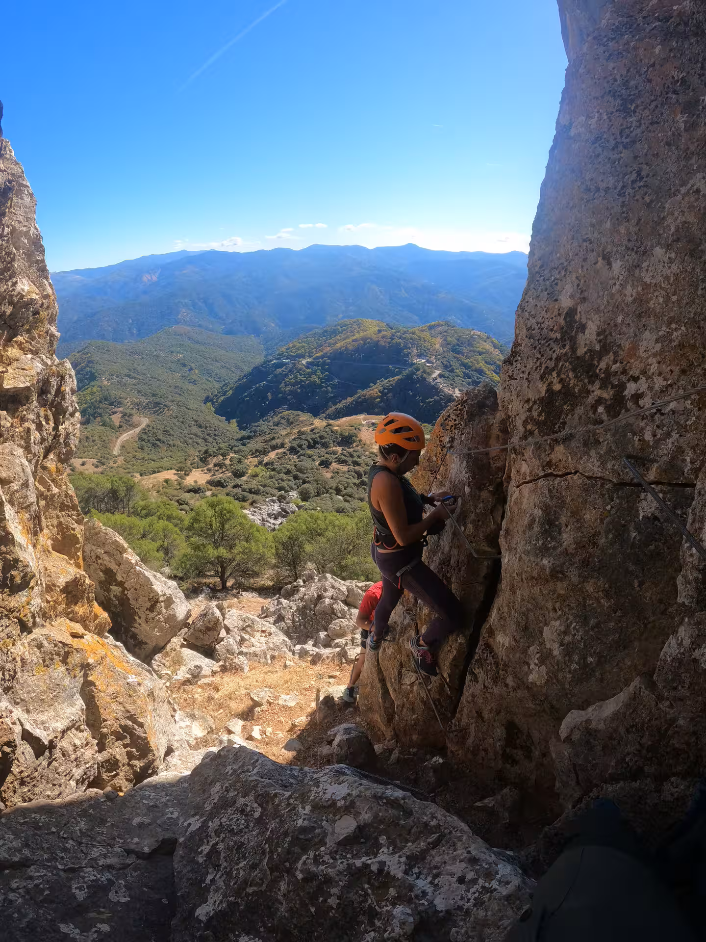 Adventurer climbs rocky Via Ferrata in Benalauría with stunning views of Costa del Sol's lush mountains.