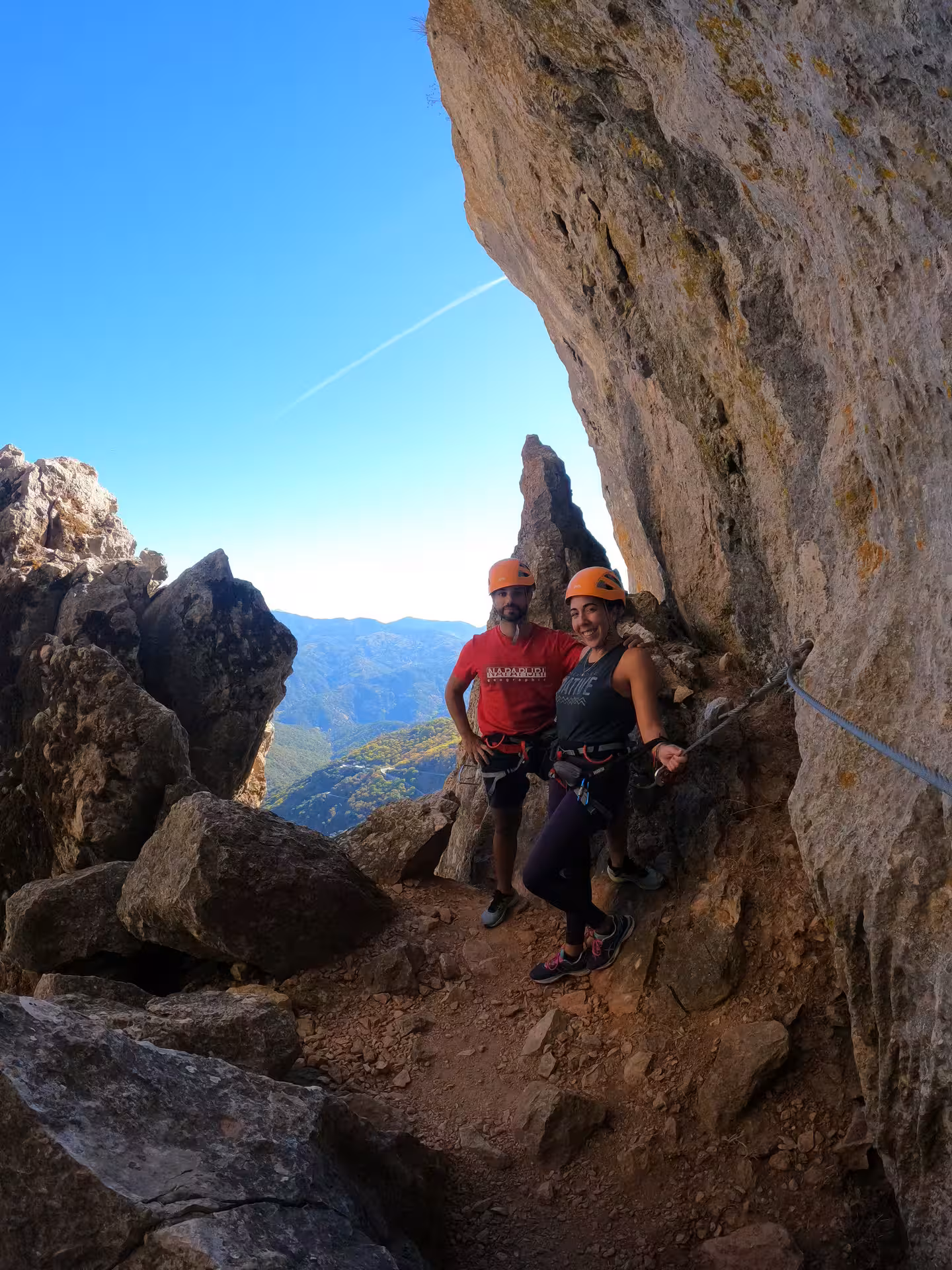 Pair of adventurers pose on Via Ferrata cliff in Benalauría, showcasing breathtaking views of Costa del Sol.