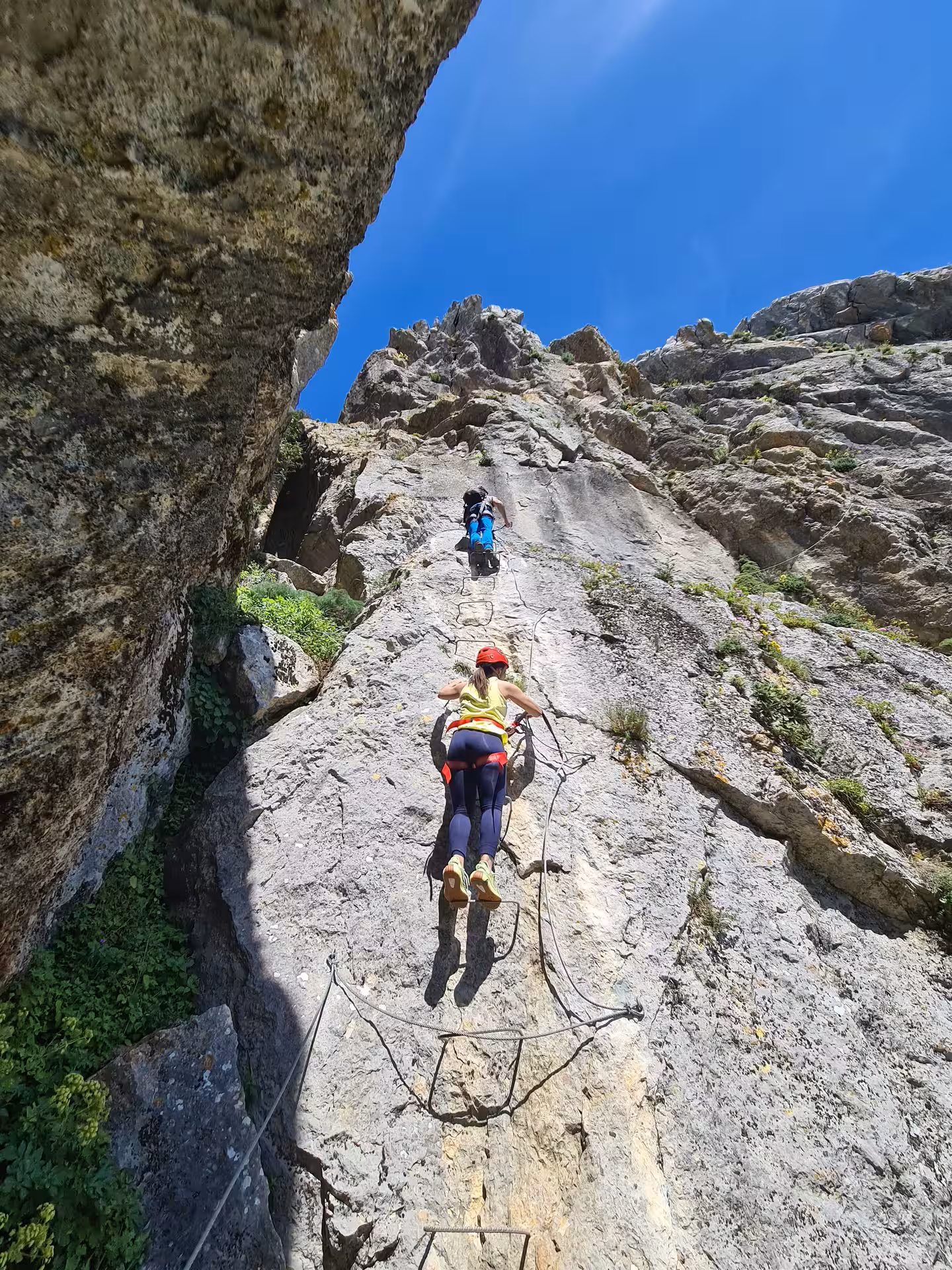 Adventurers scaling vertical cliff on Via Ferrata in Benalauría with clear blue skies, Costa del Sol.