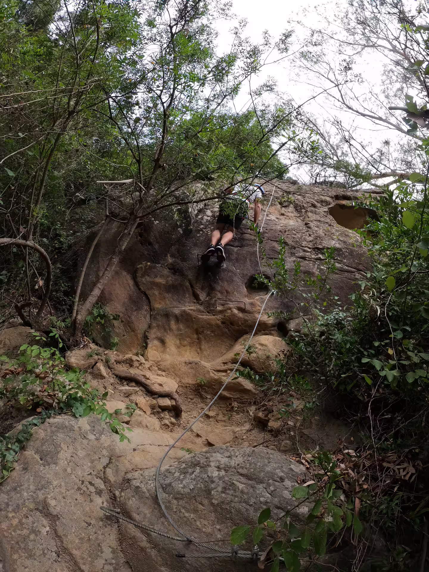 Adventurer scaling rugged terrain on Via Ferrata El Caimán, amidst the natural beauty of Alcornocales Natural Park.