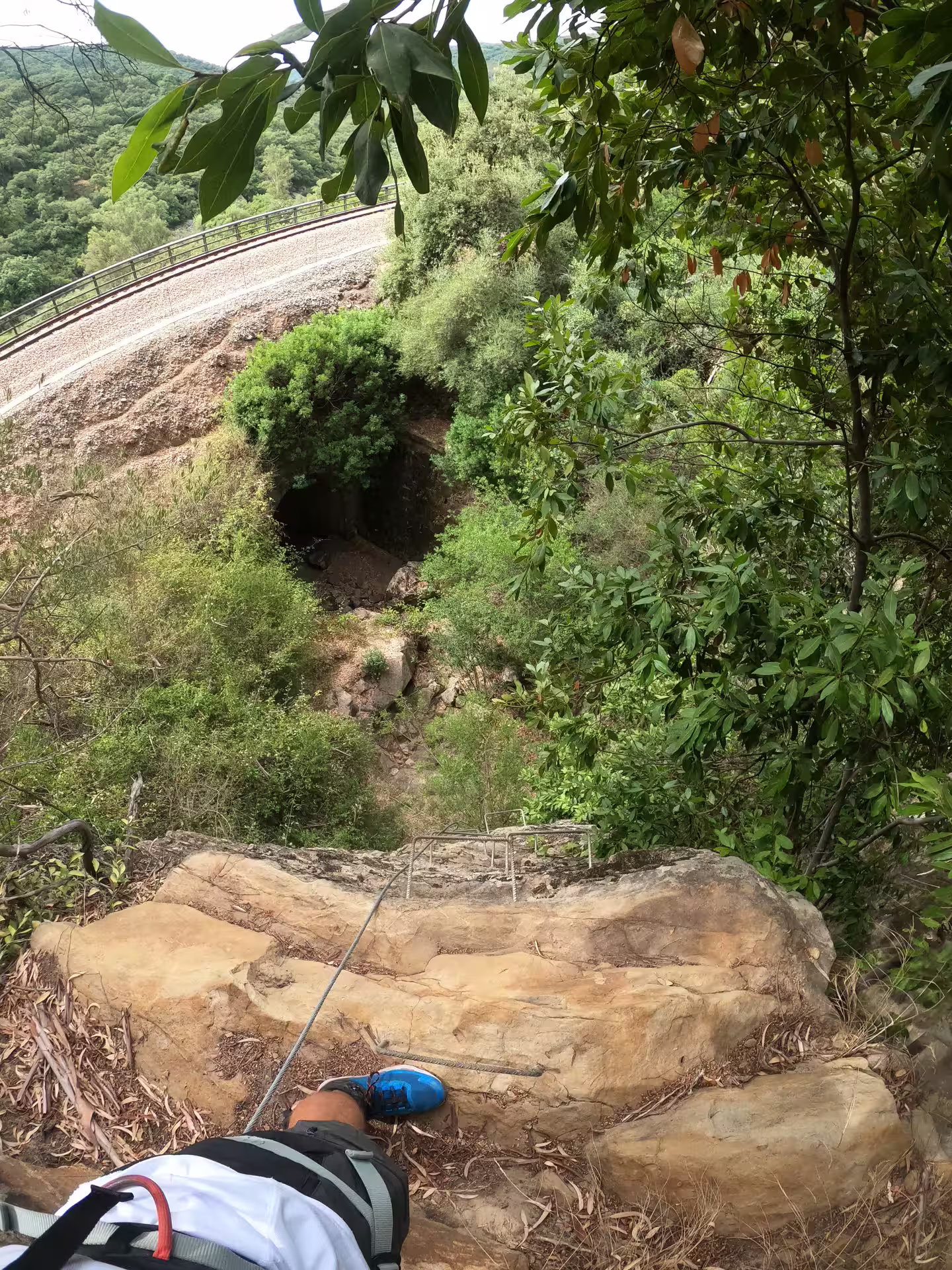View from a rocky ledge on Via Ferrata El Caimán, overlooking dense forest and a railway in Alcornocales Natural Park.