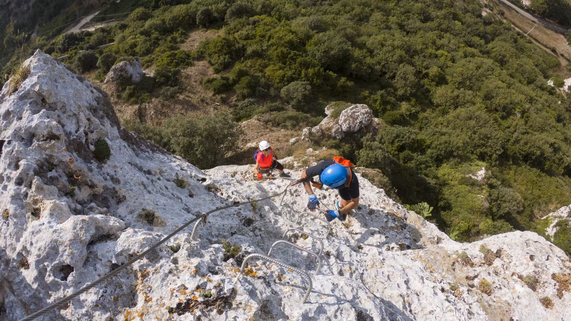 Two climbers ascending the rugged Via Ferrata di Giorré in Cargeghe, surrounded by lush green landscapes.