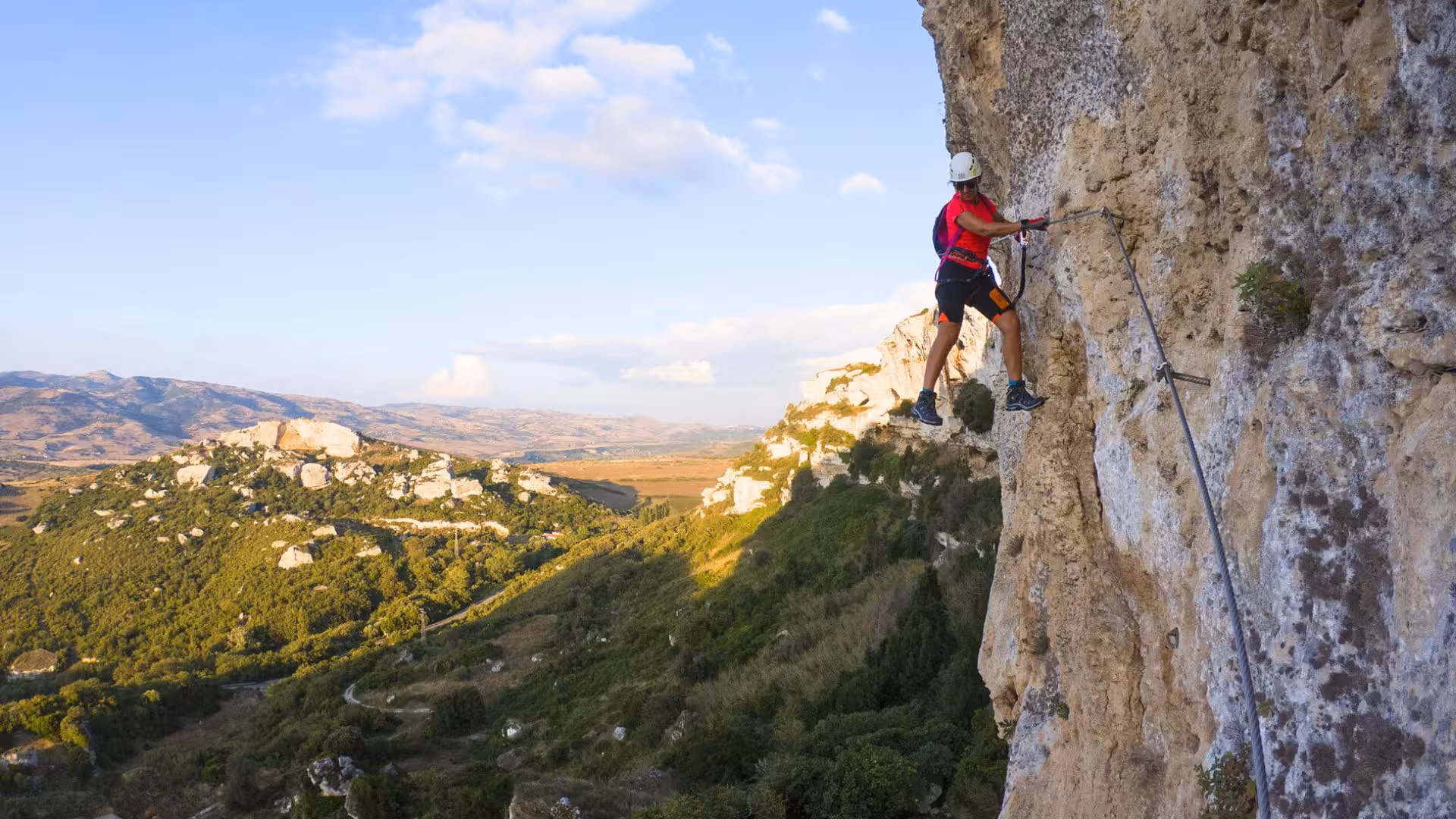 Adventurer tackles Via Ferrata di Giorré in Cargeghe, scaling a rugged cliff with panoramic Sardinian views.