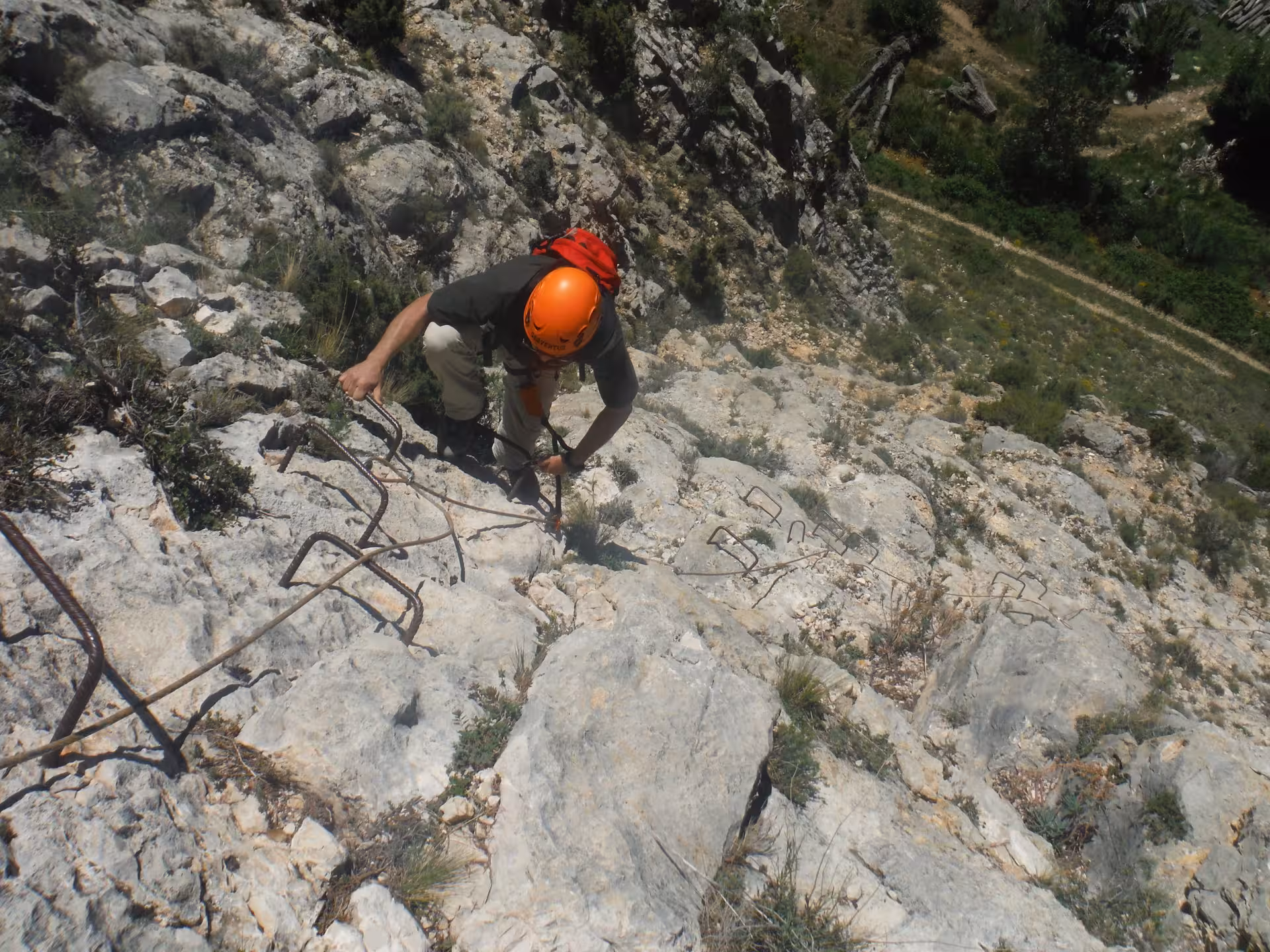 Participante con casco naranja sube por grapas en vía ferrata de iniciación en Montalbán, Teruel