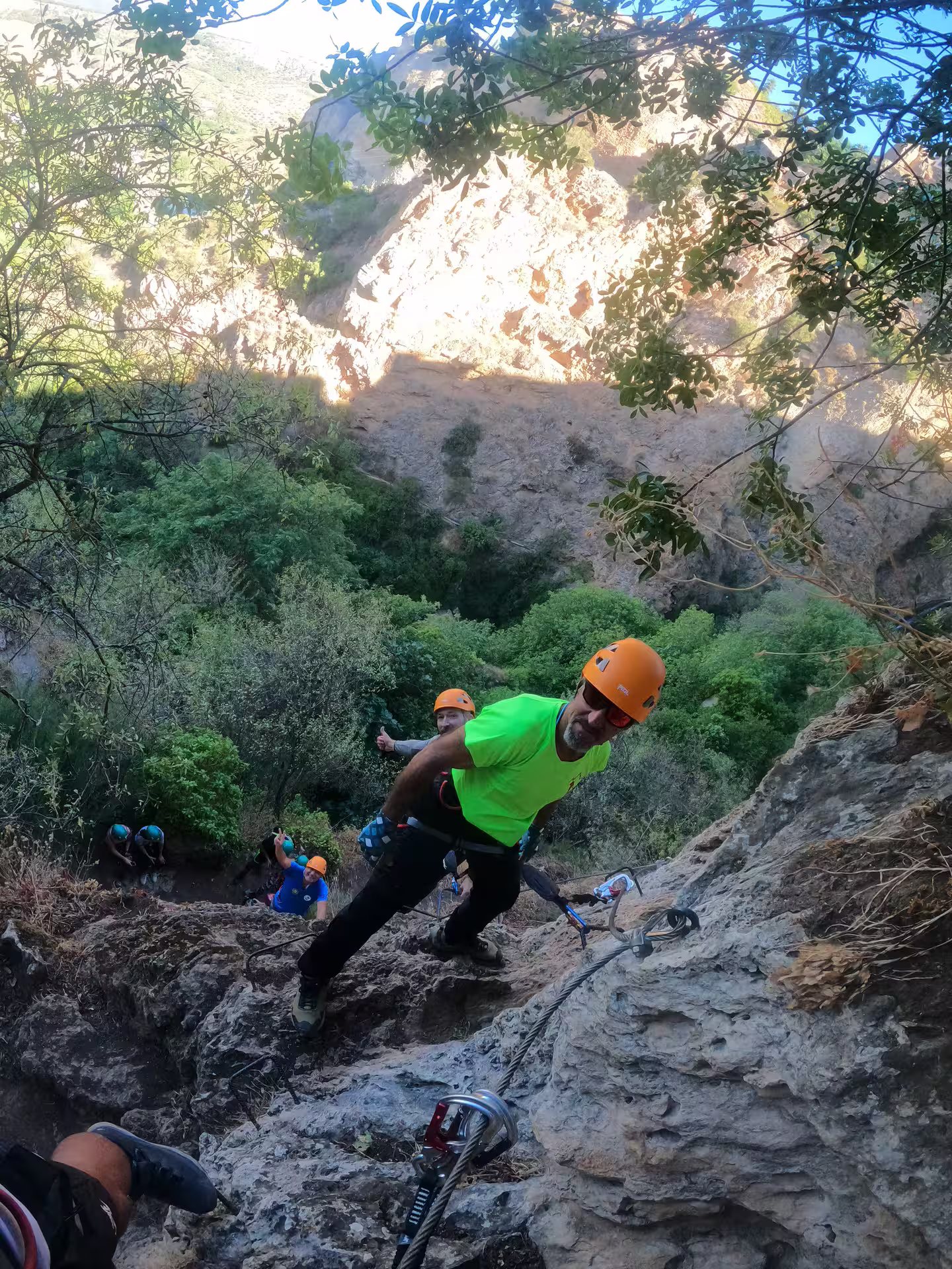 Adventurers equipped with helmets and harnesses climb a rocky via ferrata route at Tajo de Ronda under clear skies.