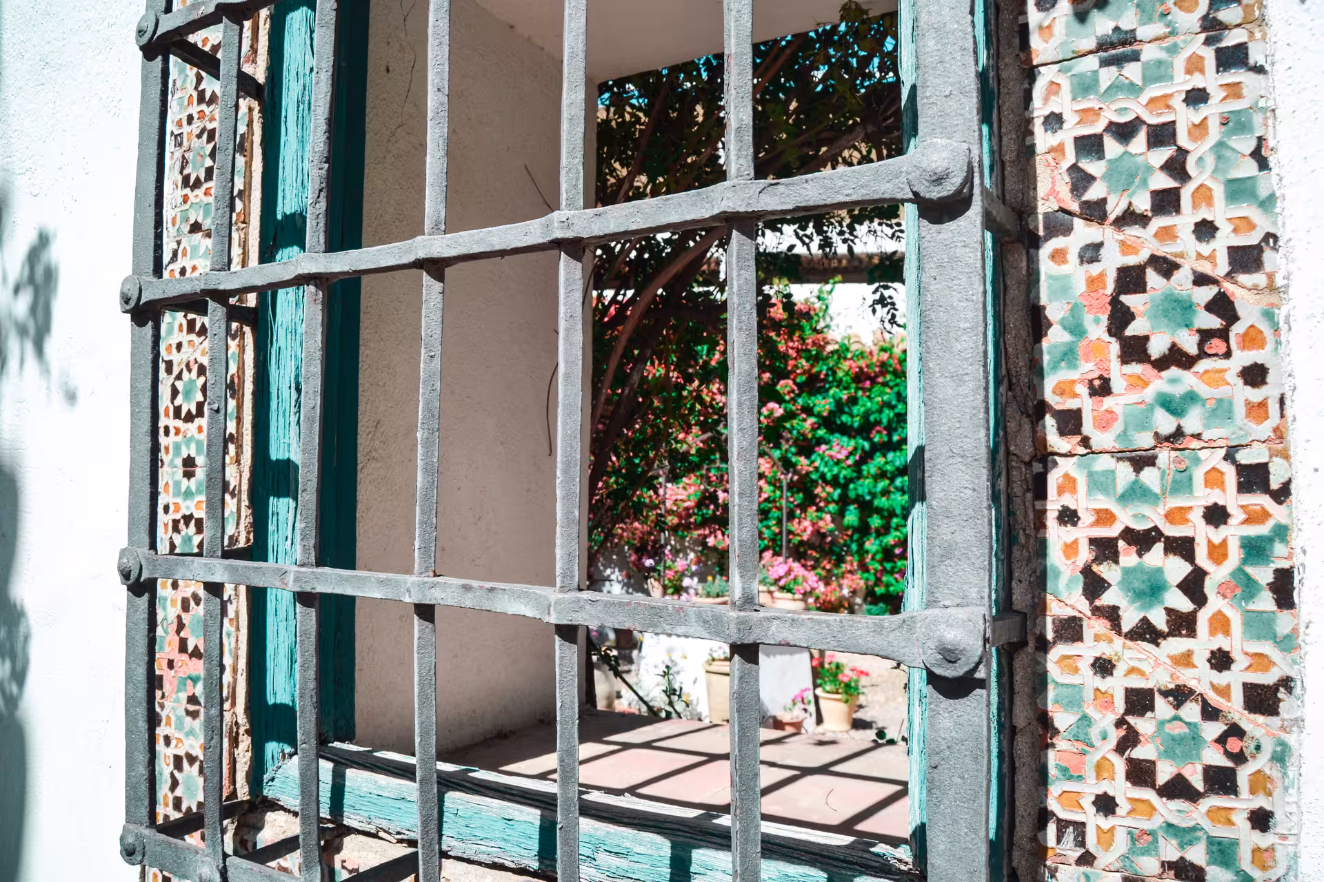 View through ornate window grill at Viana Palace courtyard with vibrant flowers and traditional tiles.