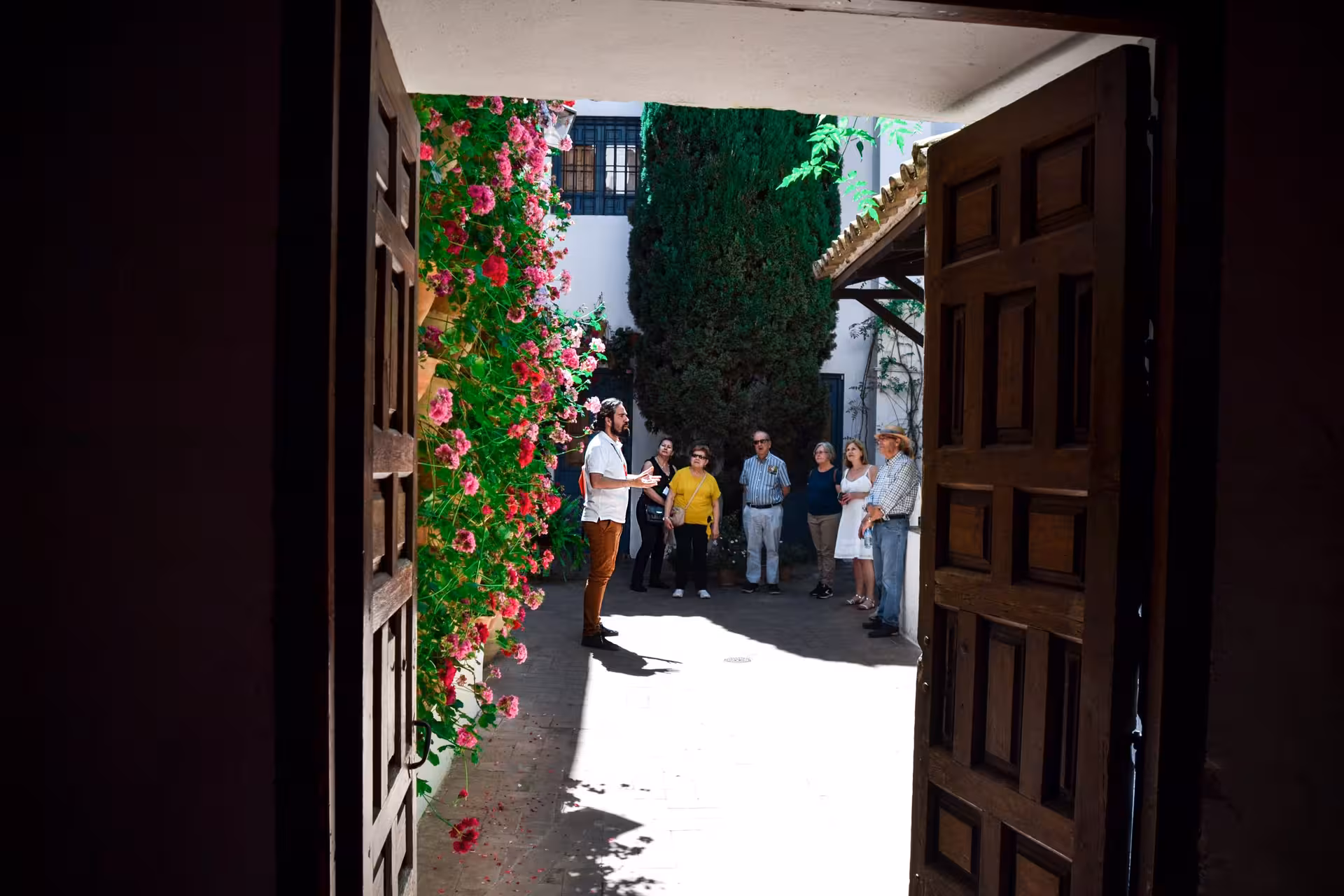 Tour group in Viana Palace courtyard with guide, surrounded by vibrant flowers and historic architecture in Cordoba.