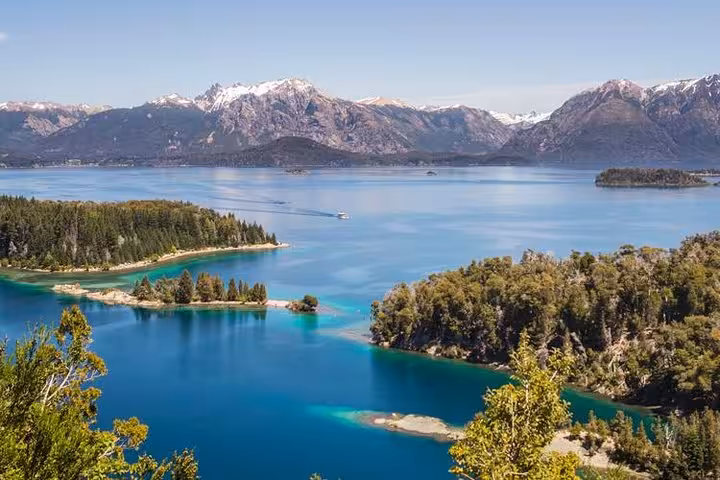 Aerial view of Victoria Island's crystal-clear waters, forested peninsulas, and distant snow-capped mountains under a clear blue sky.