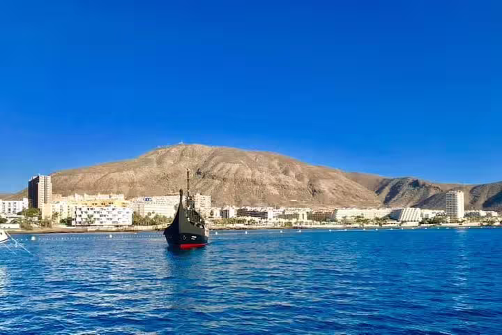 Viking ship approaches vibrant coastal town, providing scenic views and relaxation on a 3-hour cruise with drinks.