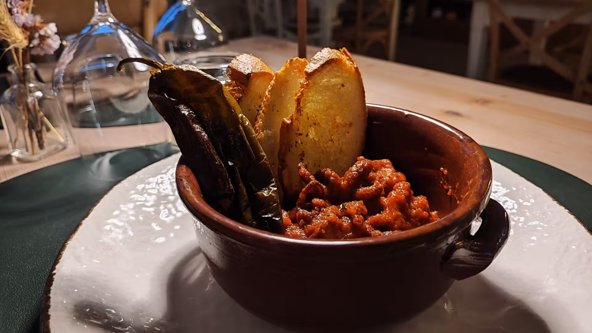 Delicious villa dinner featuring spicy stew, roasted peppers, and crusty bread in a rustic bowl setting.
