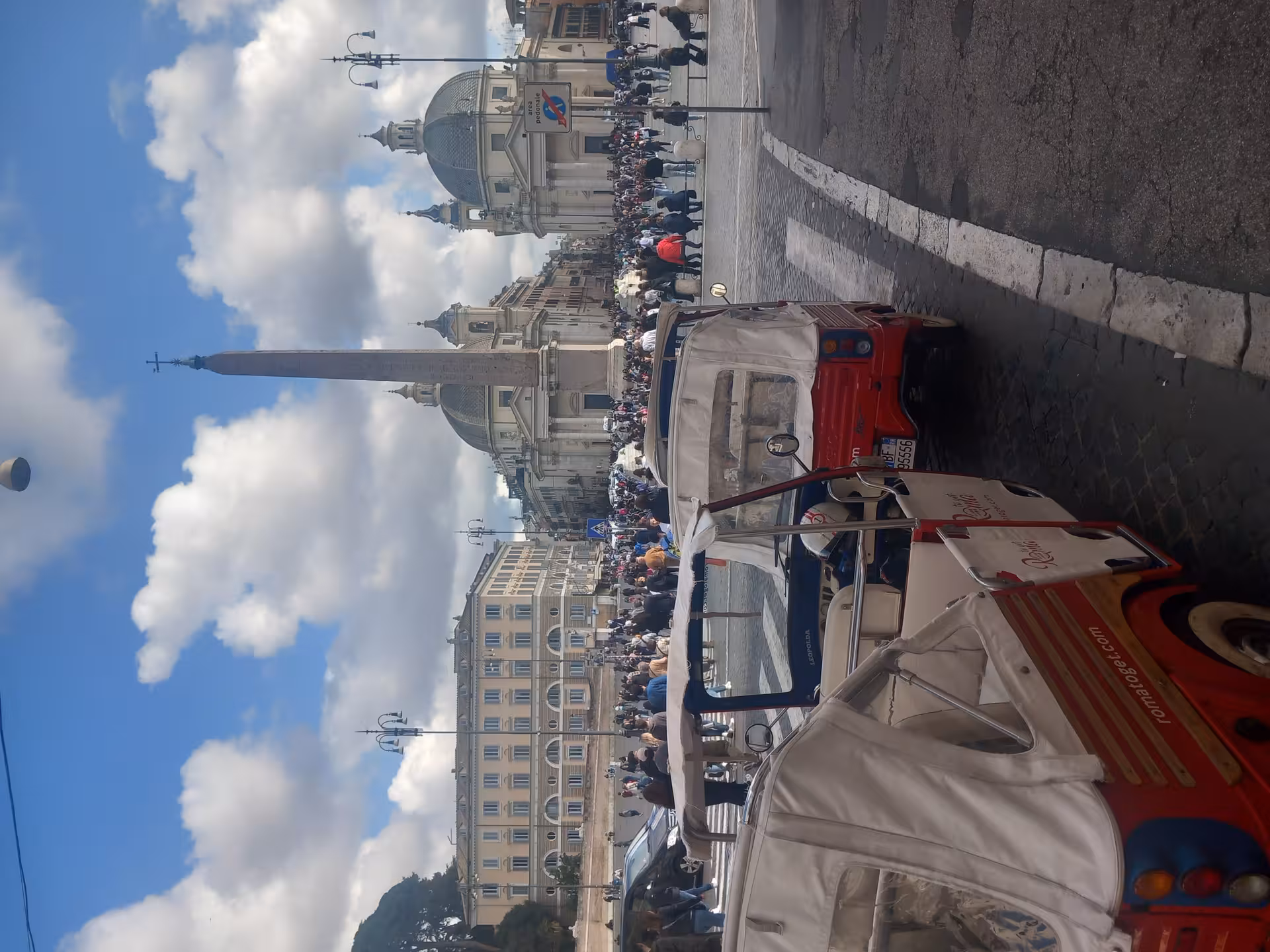Charming tuk-tuks parked near a bustling Piazza del Popolo, showcasing lively urban exploration in Rome.