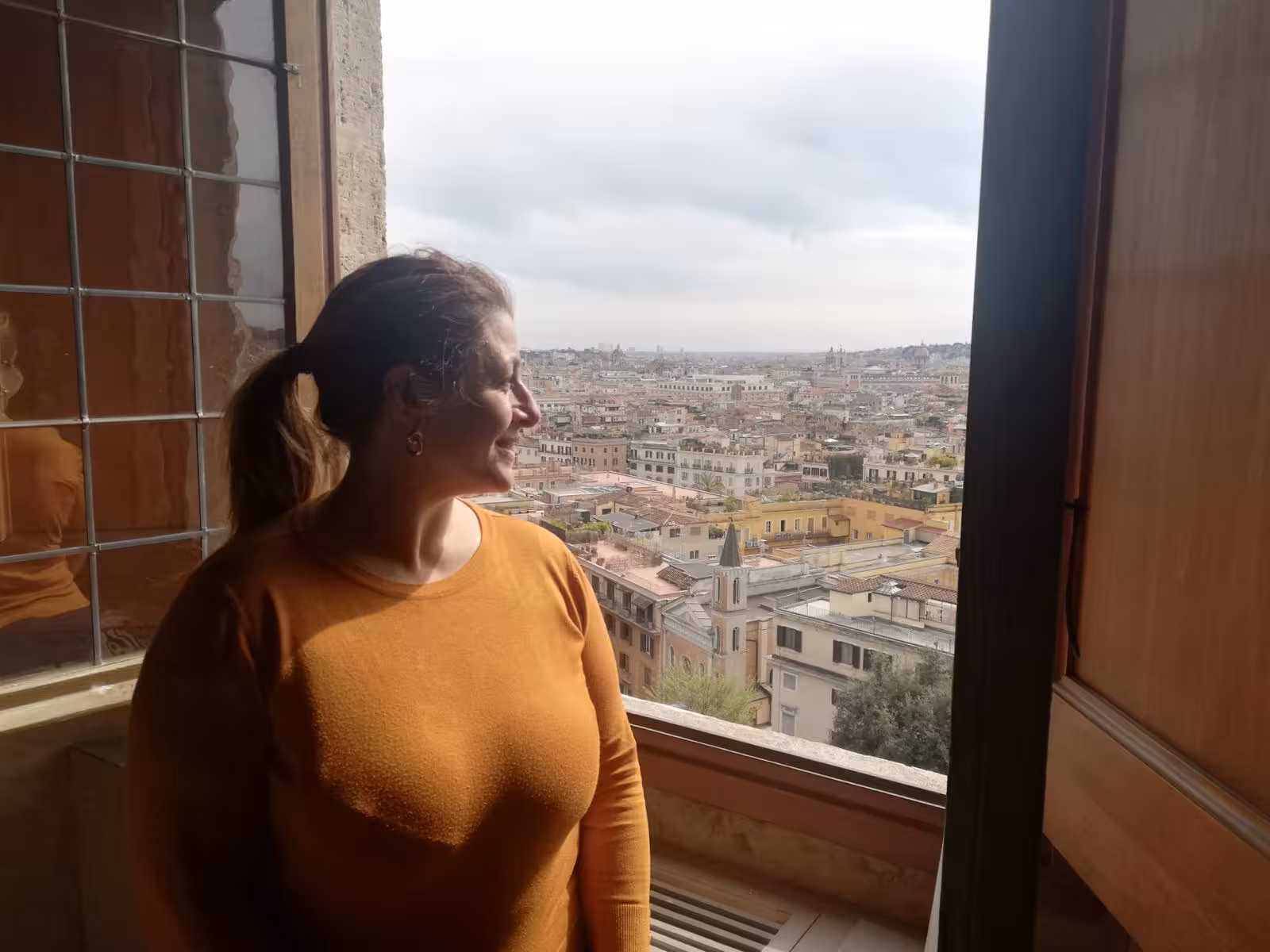 Smiling woman enjoying panoramic view of Rome from Villa Medici window on a sunny day.