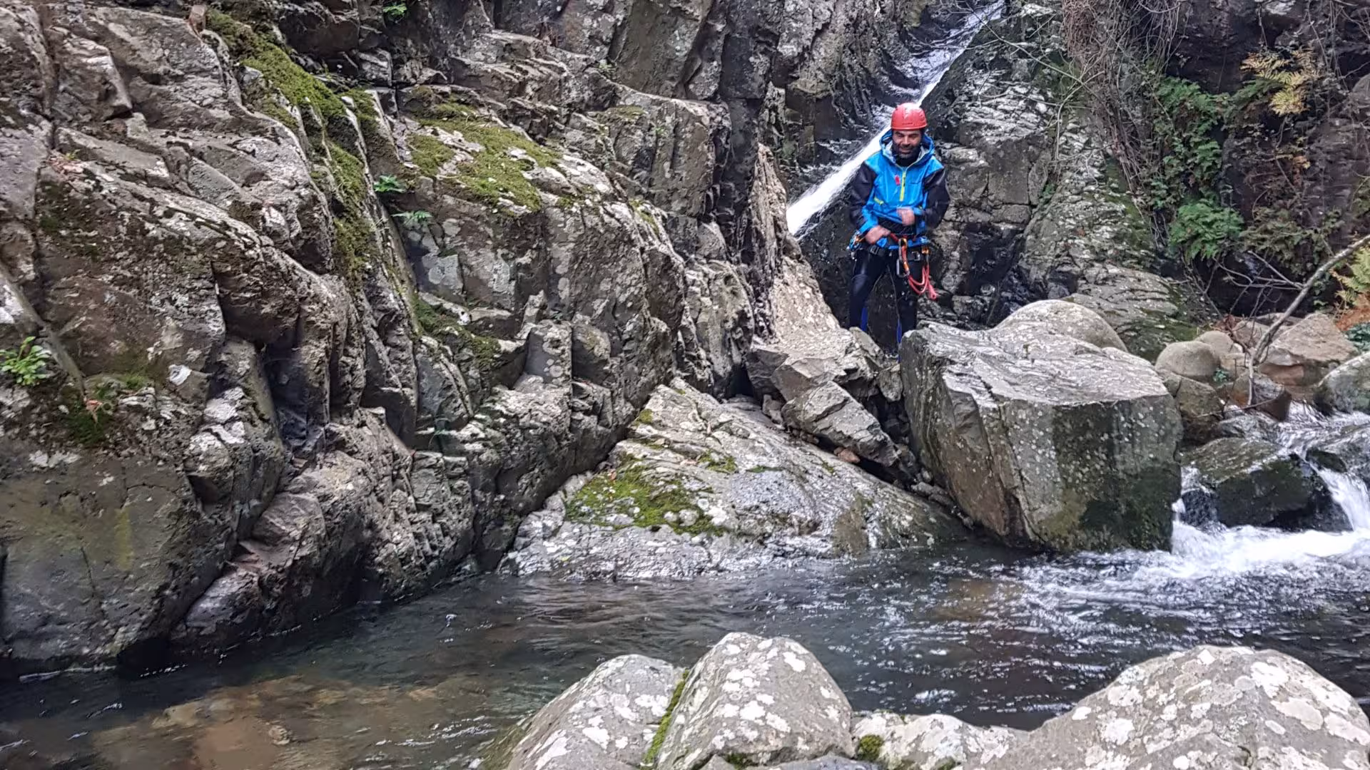 Explorer navigating rocky terrain by a stream in Villacidro's Rio Zairi canyoning adventure, wearing safety gear.