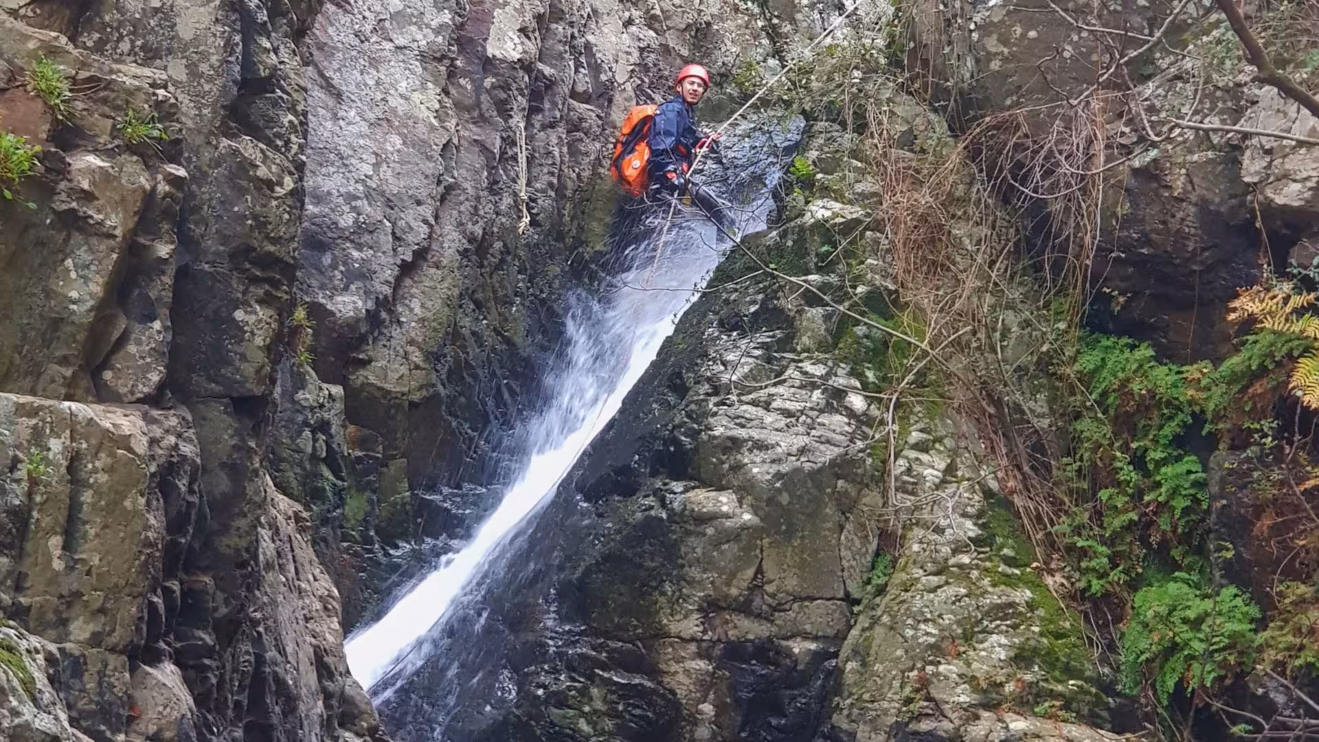 Adventurer rappelling down a waterfall in Villacidro's Rio Zairi canyoning tour, surrounded by rugged cliffs.