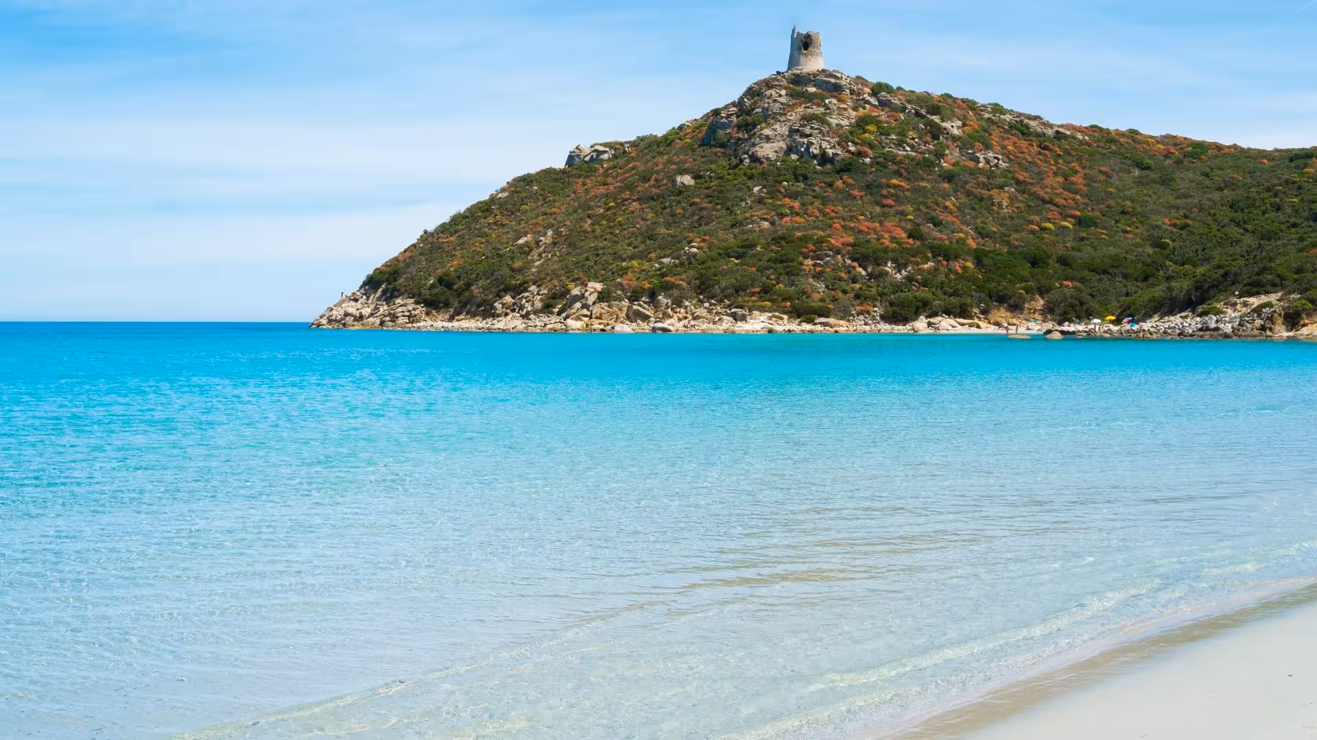 Scenic view of turquoise waters and historic tower on the hill at Villasimius beach near Cagliari, perfect for tours.