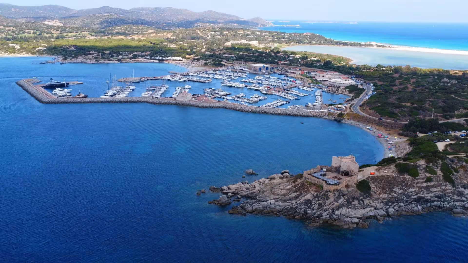 Aerial view of Villasimius marina with boats docked in crystal-clear waters, ideal for private boat tours.
