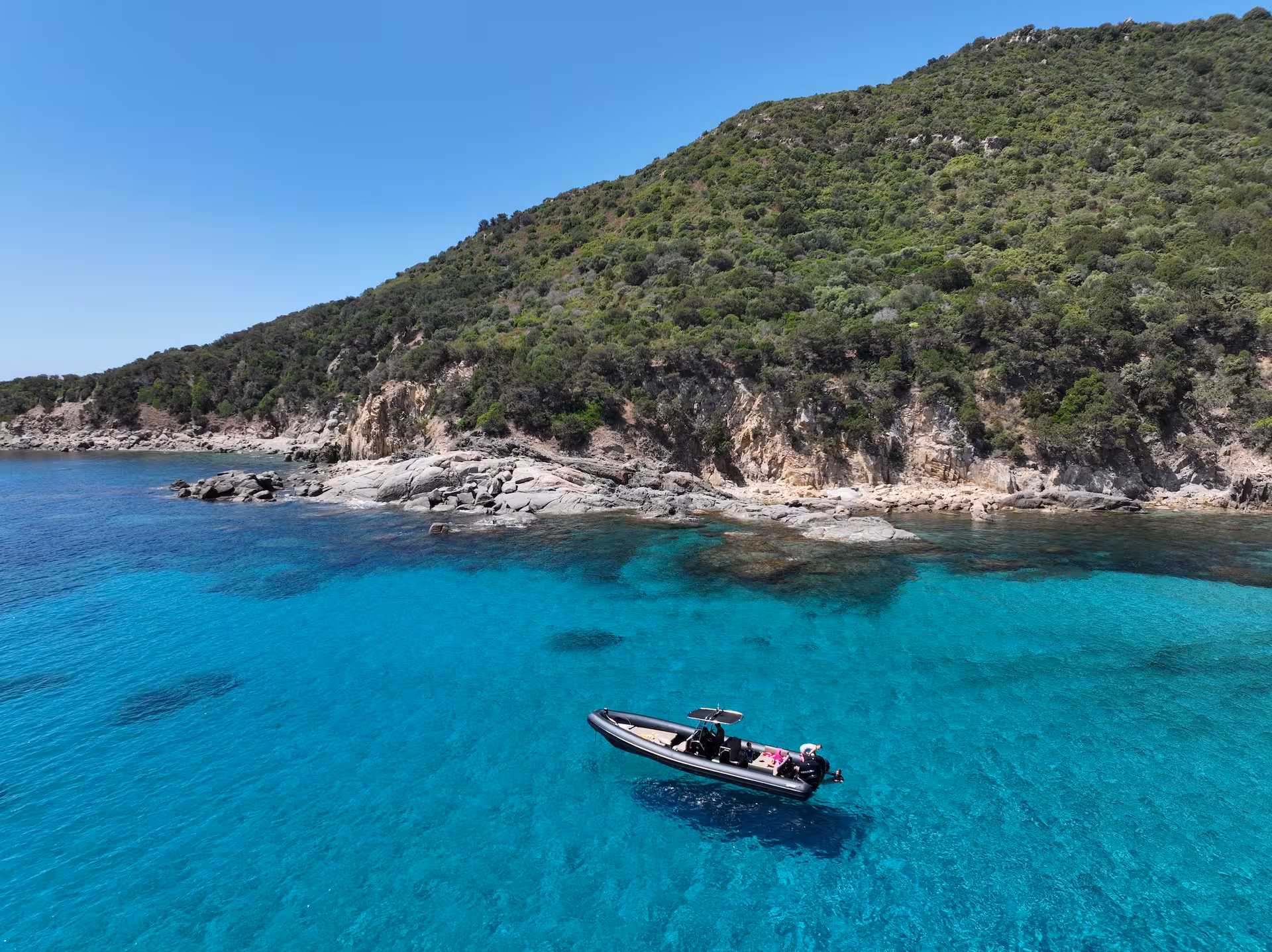 Scenic view of a maxi RIB anchored in the turquoise waters near a rocky coastline in Villasimius, ideal for swimming.