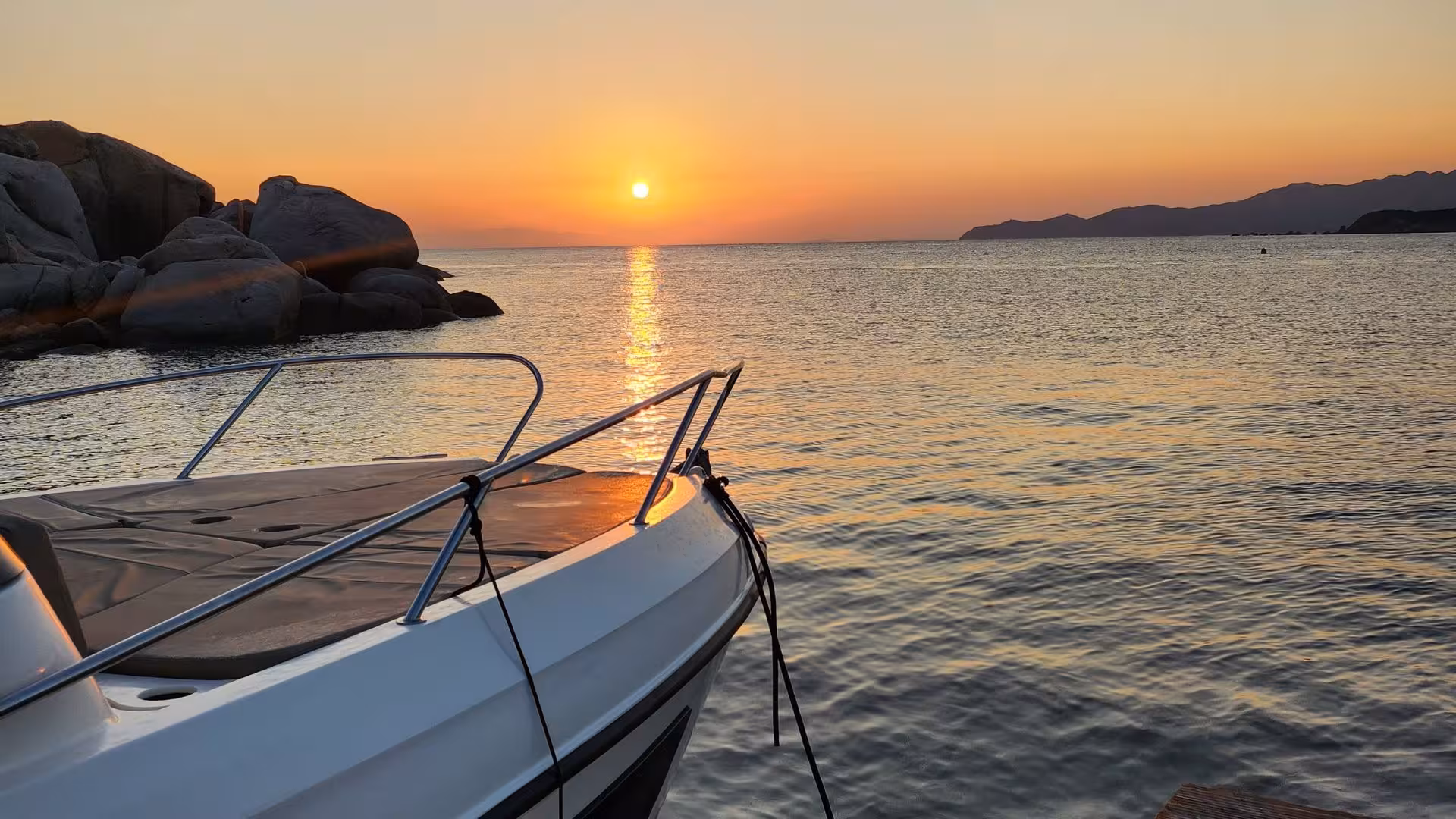Sunset view from a boat in Villasimius, highlighting serene waters and rocky coastline on a private tour.