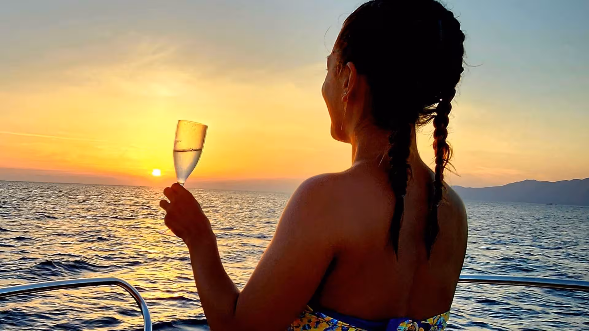 Woman enjoying a champagne toast on a sunset boat tour in Villasimius, showcasing stunning ocean views.