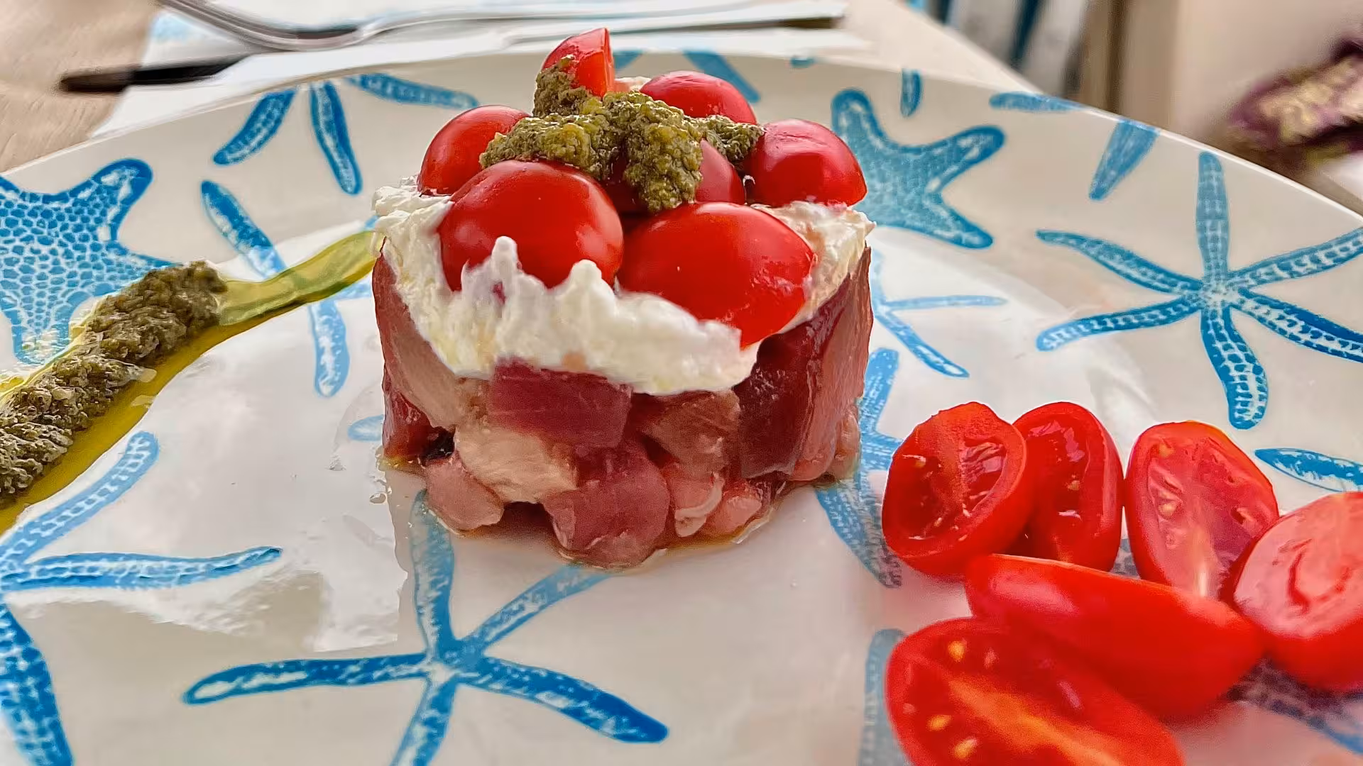 Gourmet dish with fresh tuna, cherry tomatoes, and pesto on a starfish-patterned plate during Villasimius yacht tour.