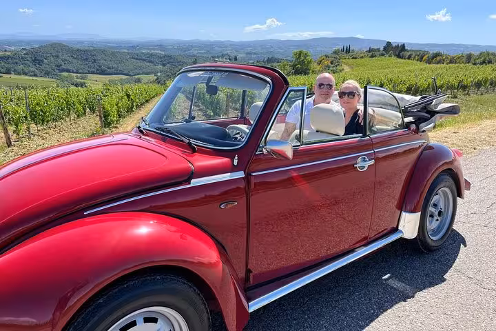Couple enjoying a ride in a red vintage Beetle amidst Tuscany's rolling vineyard hills.
