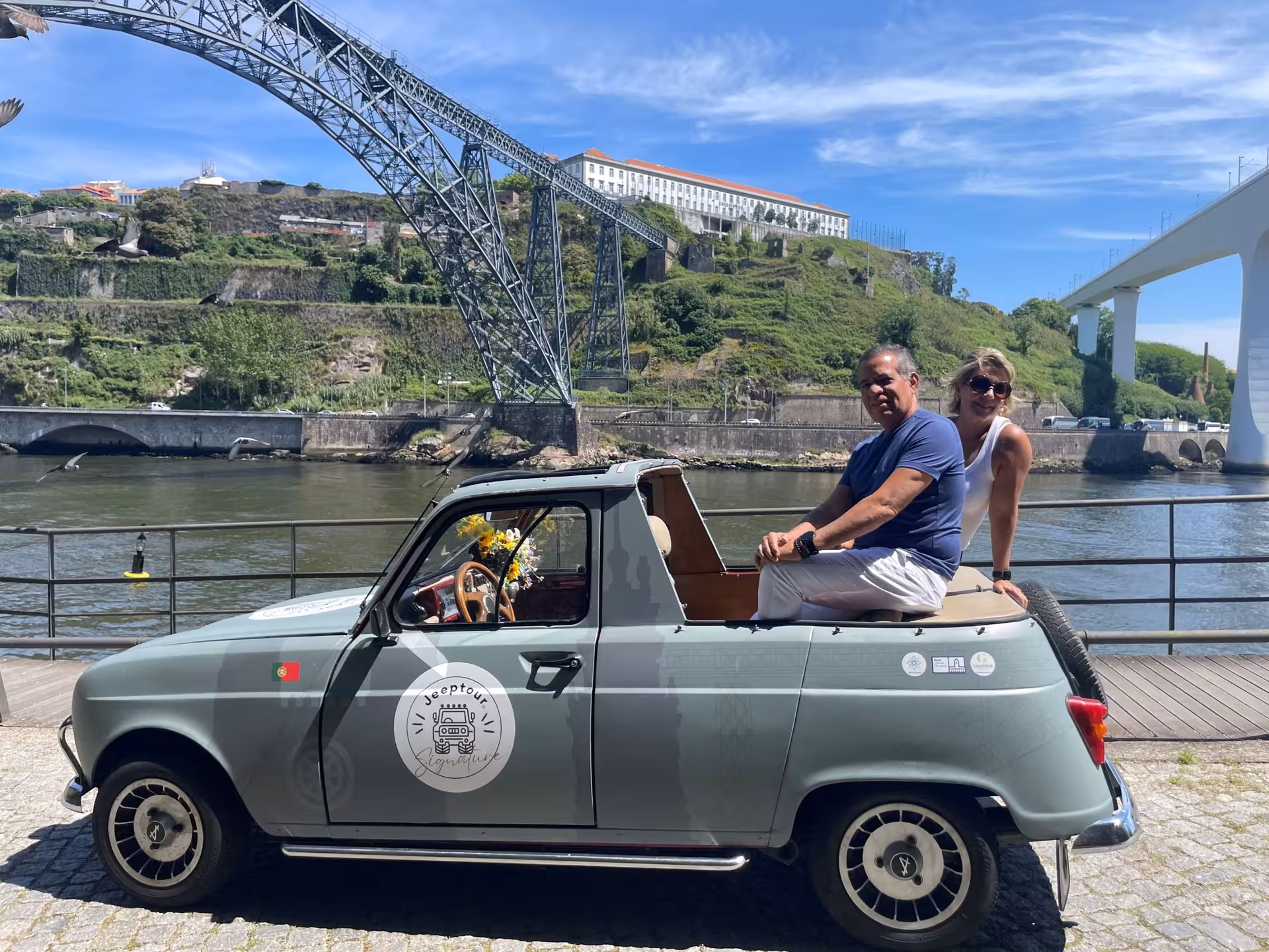 Couple in a vintage convertible by the Douro River under Dom Luís I Bridge, Porto and Gaia sightseeing tour