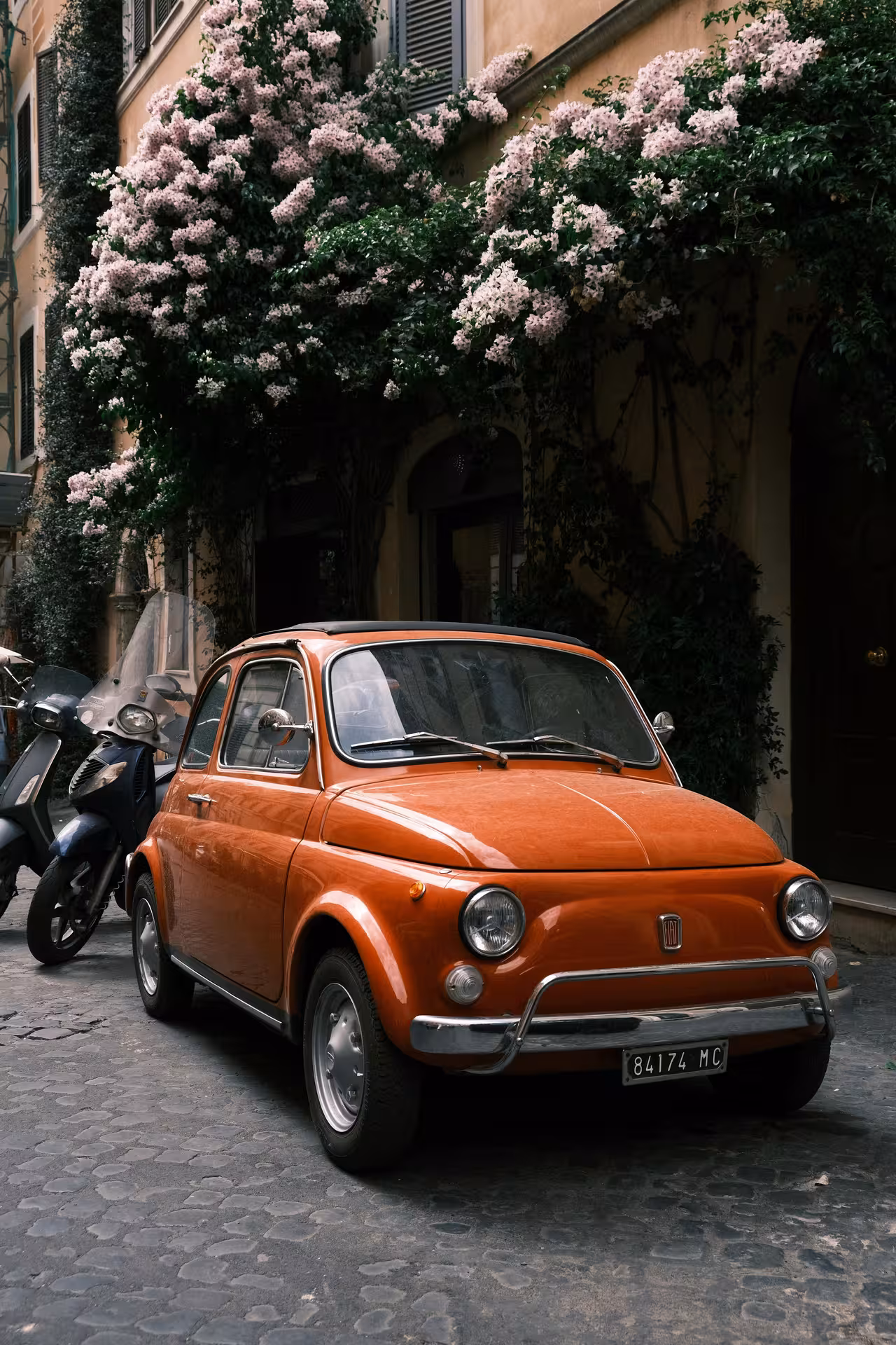 Vintage orange Fiat '500 parked on a charming cobblestone street, perfect for an Ancient Ostia tour experience.