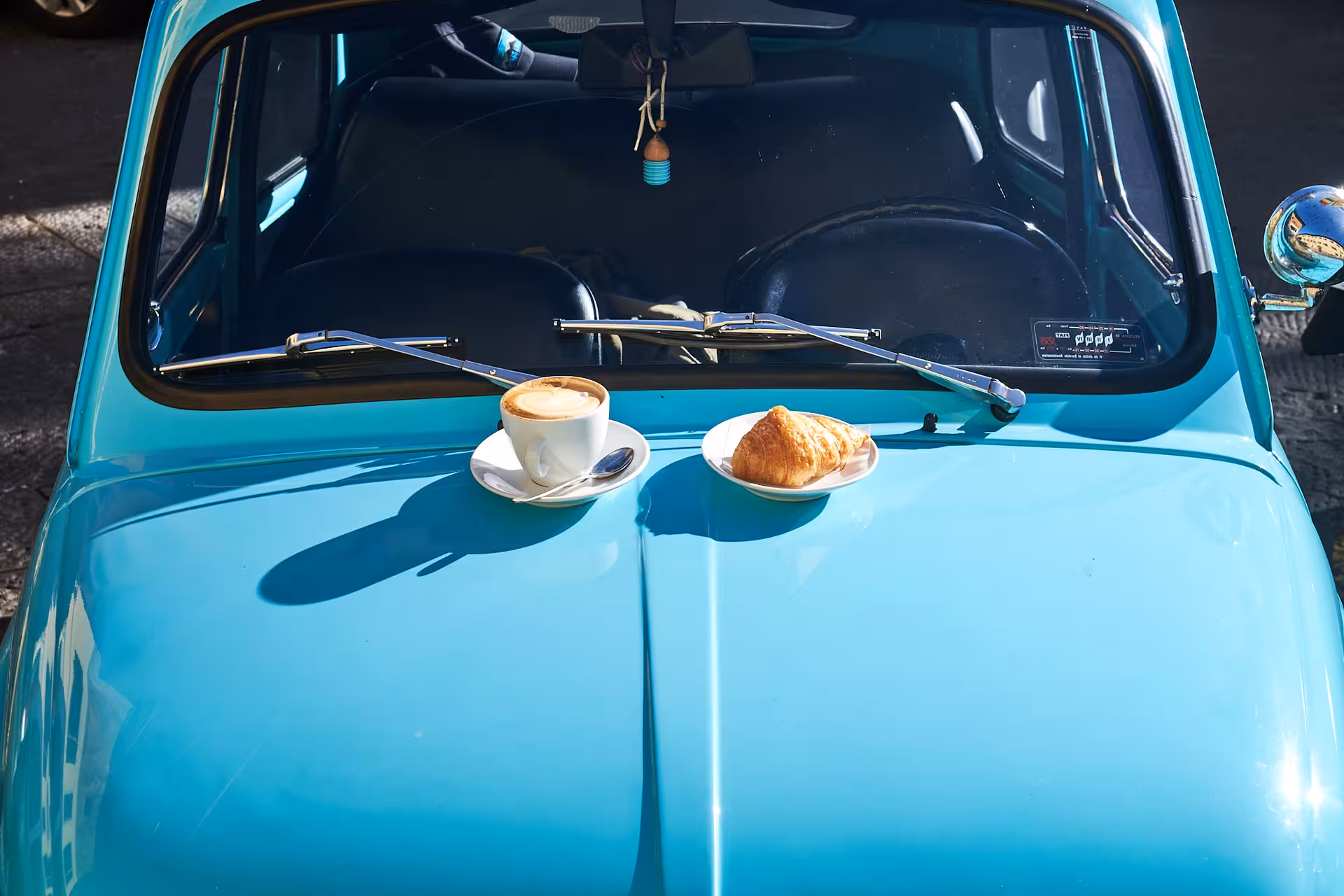 Cup of cappuccino and croissant on the hood of a turquoise vintage FIAT 500 in Tuscany.