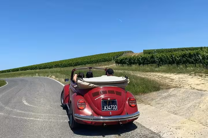 Vintage red Beetle cruising through picturesque Tuscany routes, offering a unique wine tour experience.