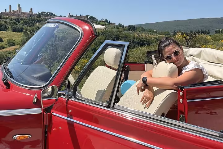 Woman relaxing in a vintage red Beetle car during a scenic Tuscany tour with lush vineyard views.