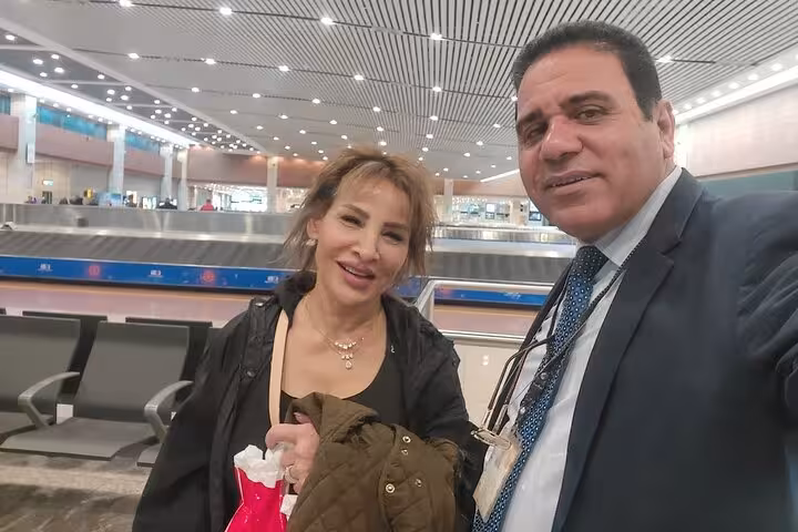 Two travelers at Cairo Airport's baggage claim enjoying VIP meet and assist service with a welcoming guide.
