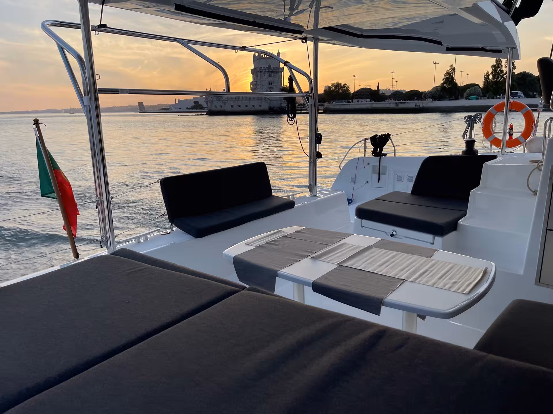 VIP catamaran cockpit with lounge seating and table, sailing past Belem Tower at sunset in Lisbon