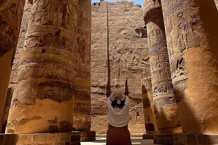 Visitor raises arms amidst the colossal, hieroglyph-covered columns of Karnak Temple in Luxor, Egypt.