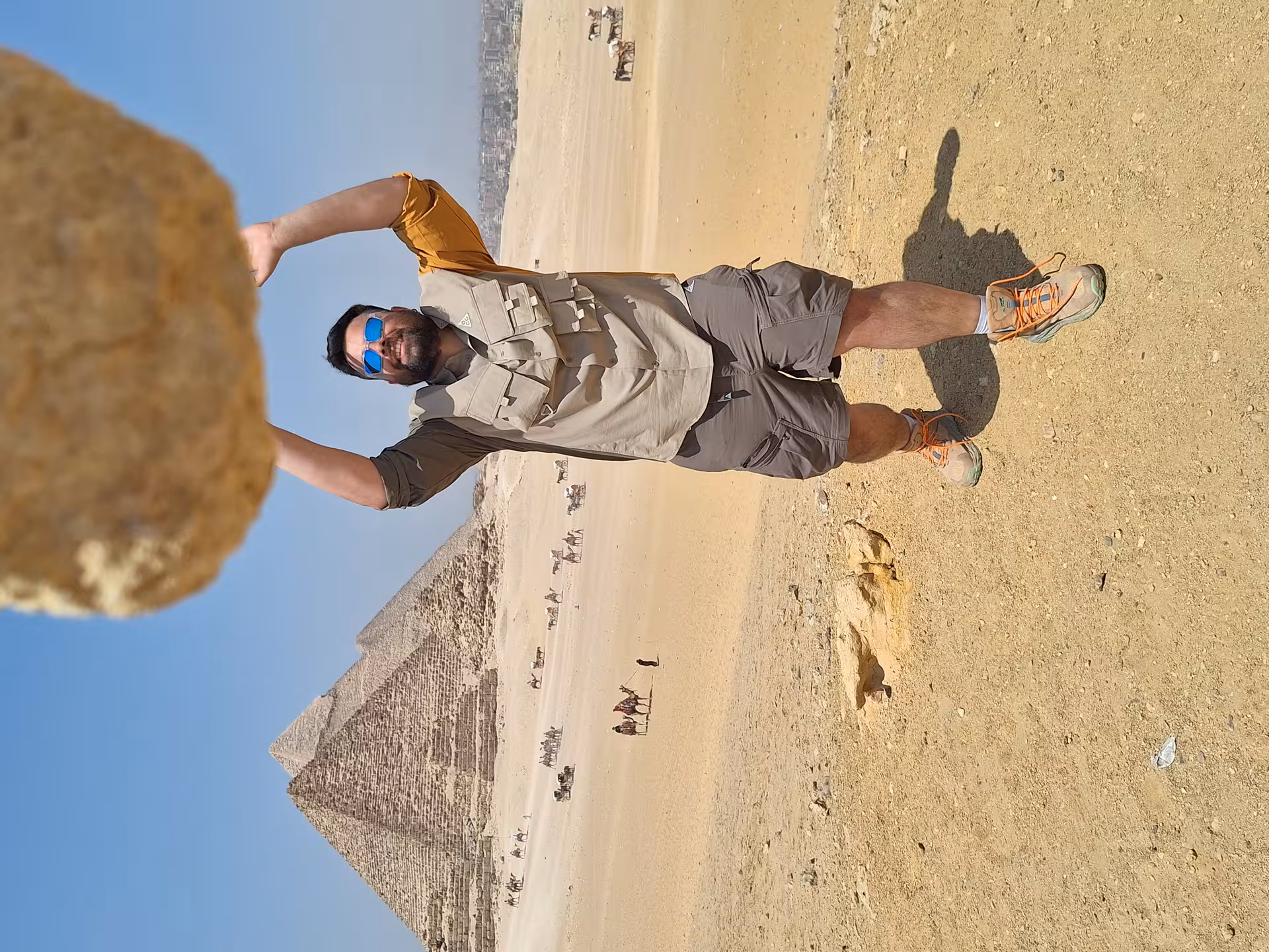 Visitor posing with a large rock and the Pyramid of Giza, showcasing the unique desert experience in Cairo, Egypt.