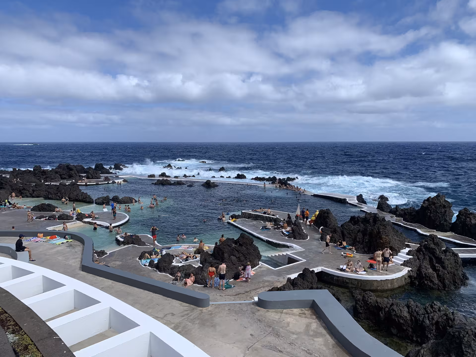 Natural volcanic swimming pools by the ocean, attracting visitors on a sunny day, perfect for private group relaxation.