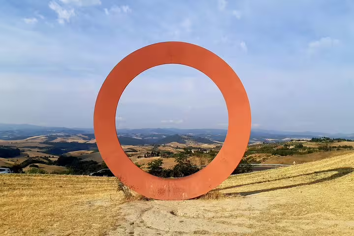 Contemporary red ring sculpture framing rolling Tuscan hills near Volterra on a private shore excursion from Livorno Port