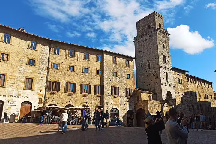 Travelers explore a sunny medieval square in San Gimignano, Tuscany on a private Volterra and wine tasting day tour