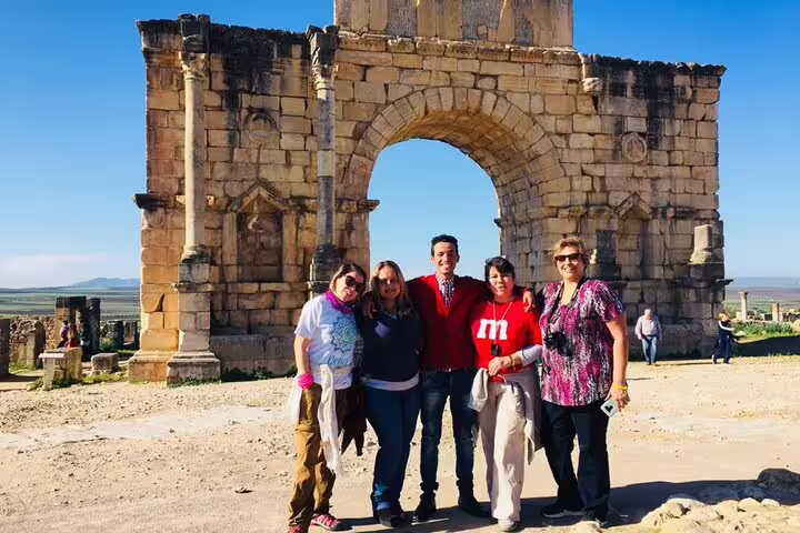 Travelers pose at the Volubilis Roman ruins arch on a Morocco 12-day tour from Casablanca to Meknes