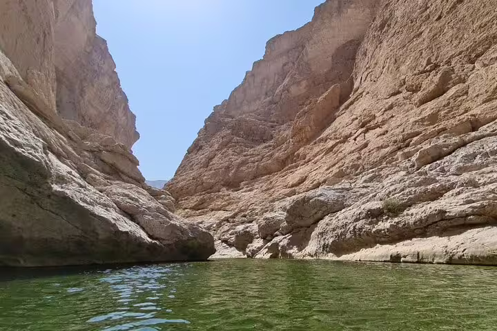 Majestic canyon walls tower over the tranquil green waters of Wadi Al Arbeieen, offering a stunning natural vista.