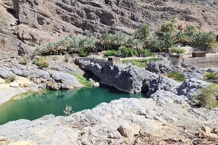 Crystal-clear water pool surrounded by rocky terrain and palm trees at Wadi Al Arbeieen, a highlight of Oman tours.