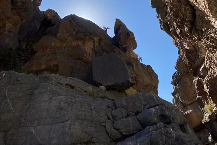Adventurer atop towering rock formations in Wadi Dham under clear blue skies, highlighting natural beauty of Oman canyon.