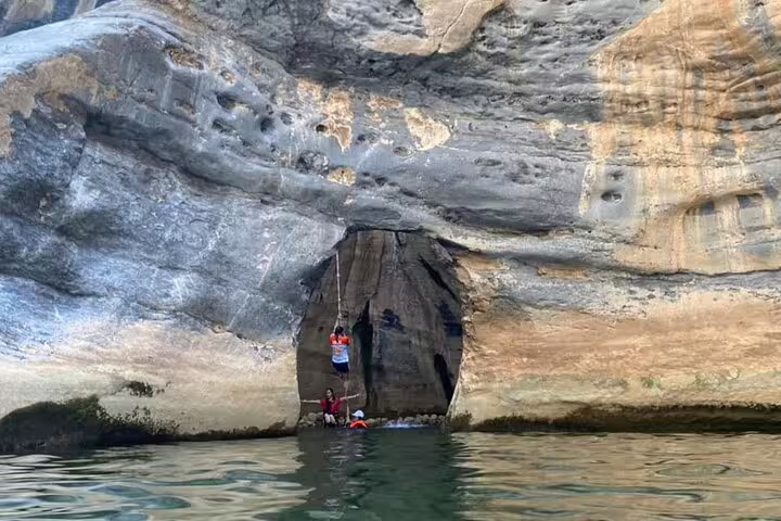 Explorers climbing through a rocky crevice with water at the base during a Wadi Dham adventure.