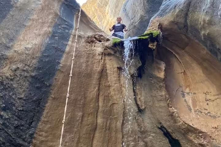 Adventurer standing atop a rocky ledge with a small waterfall on a Wadi Dham tour.