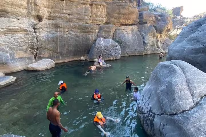 Group of tourists swimming and exploring rocky canyon pool in Wadi Dham, highlighting adventure and natural beauty.